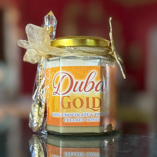 Jar of Dubai Chocolate Bar Gold Edition Creamed Honey with pistachio, white chocolate ganache, and edible gold leaf, styled with gold spoon